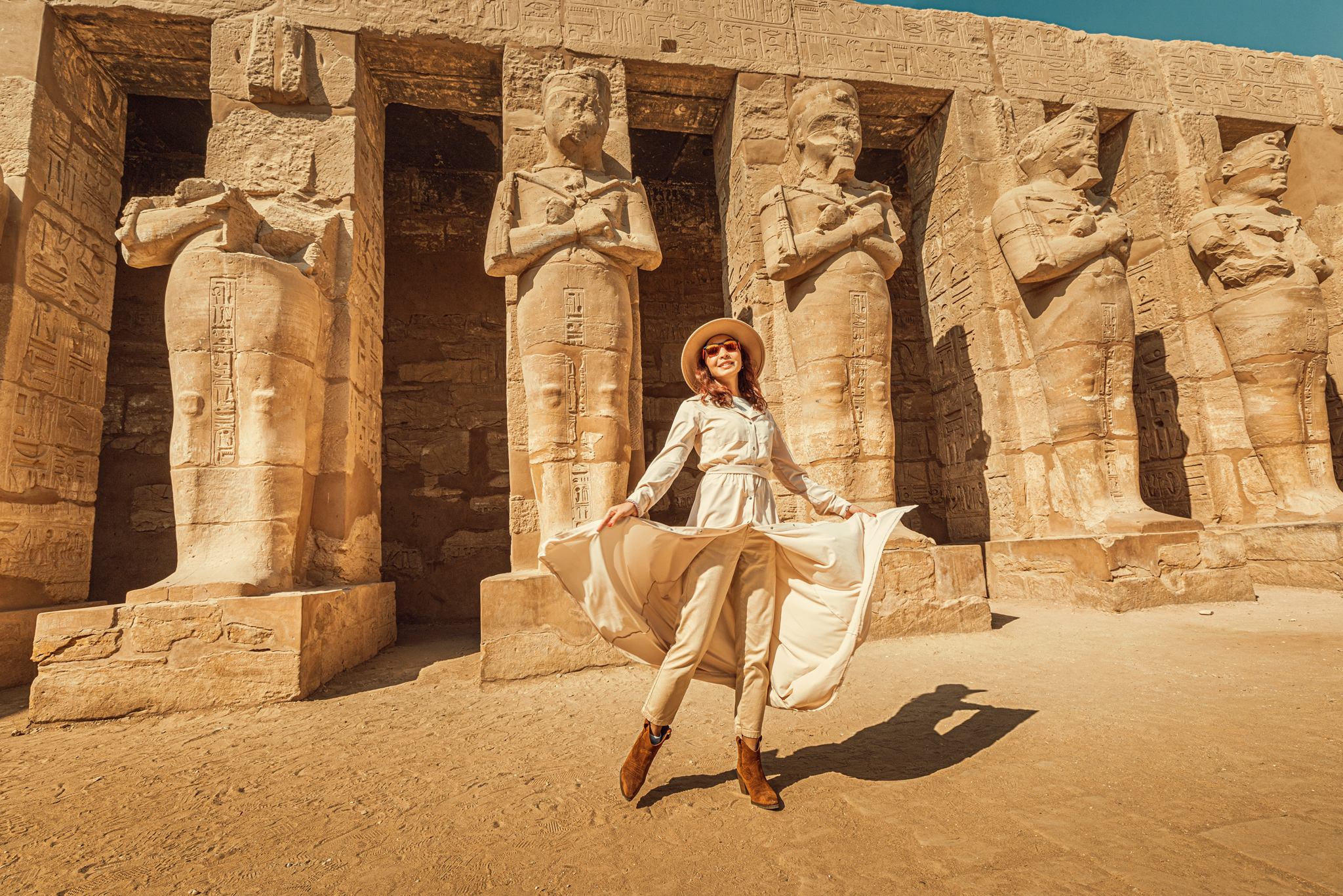 A happy tourist girl in a dress is interested in Egyptology and archaeology and gets a travel experience at the Karnak Temple in Luxor.