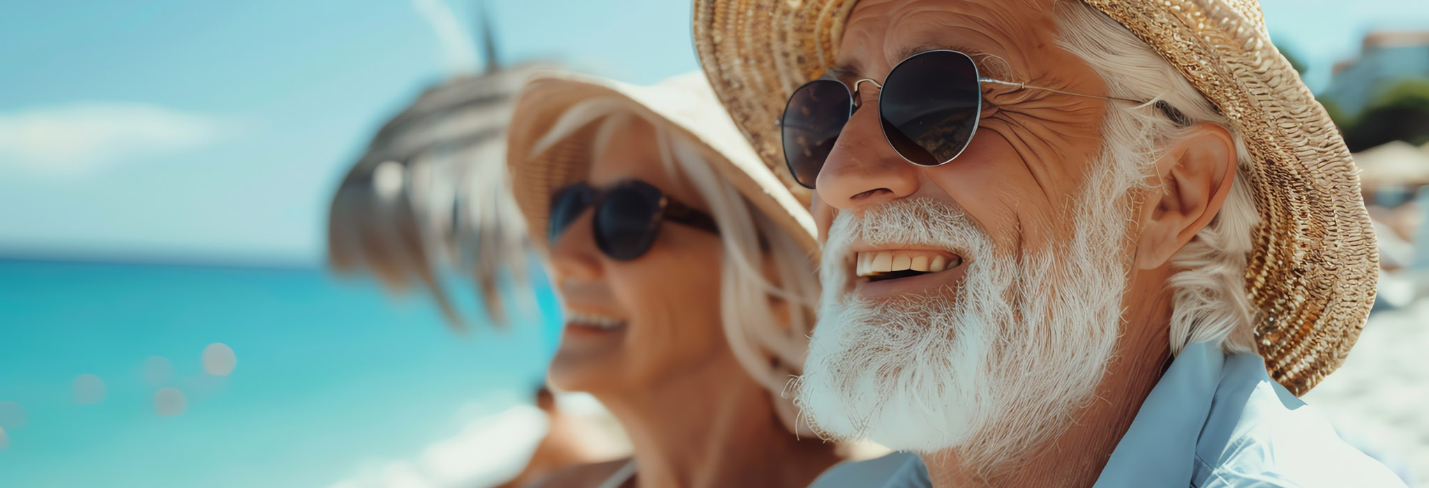 Happy senior couple relaxing on the beach. They are both wearing hats and sunglasses and they are smiling.