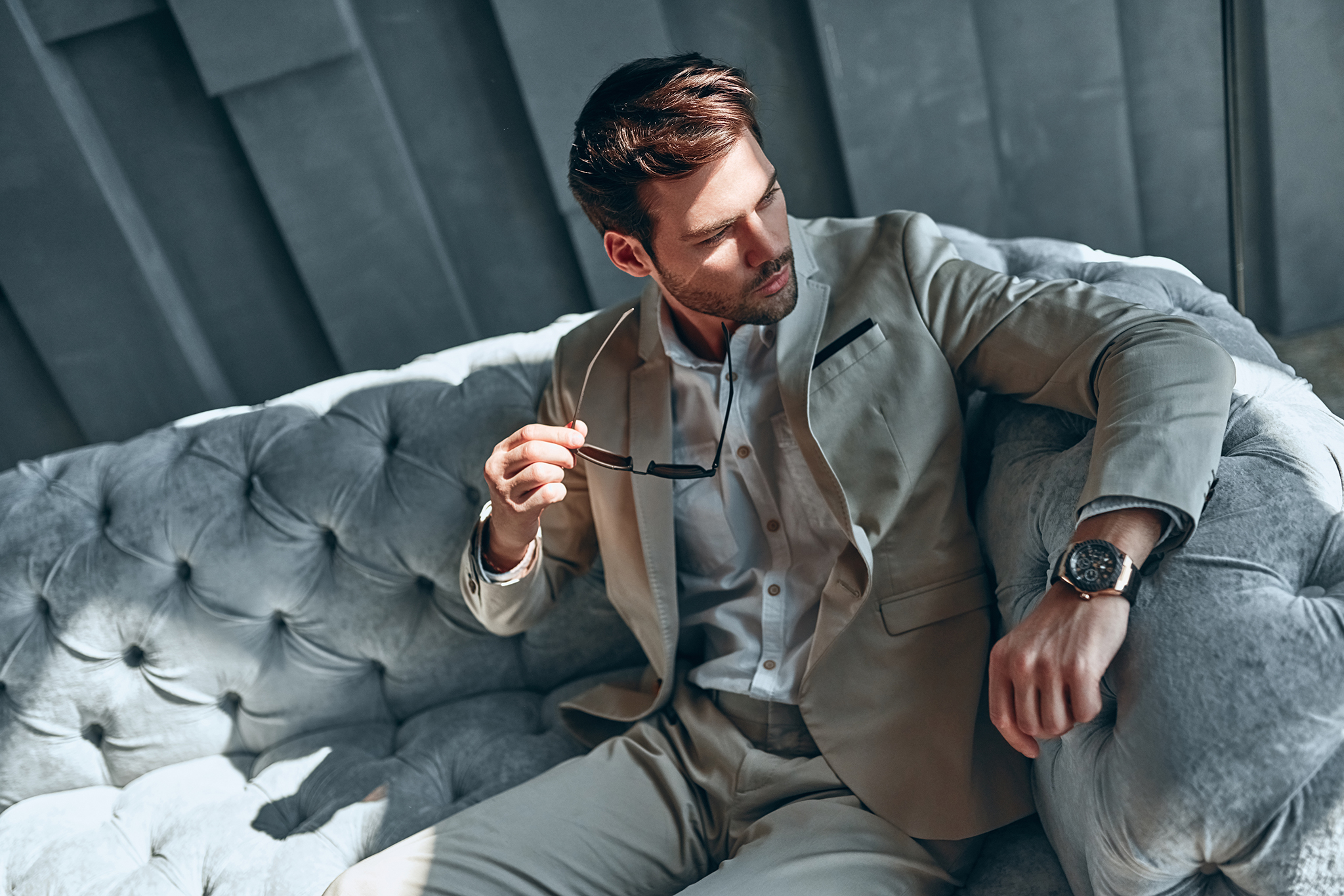 Handsome stylish man in beige suit at home sitting on sofa.