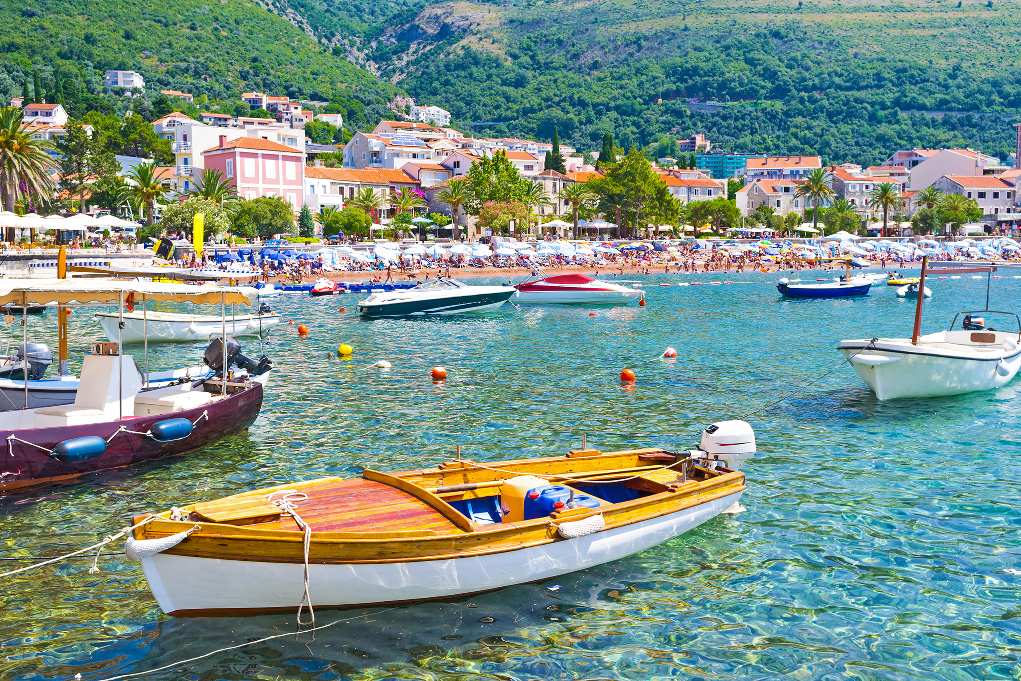 The small boats in moored harbor with the public beach on the background, Petrovac, Montenegro.